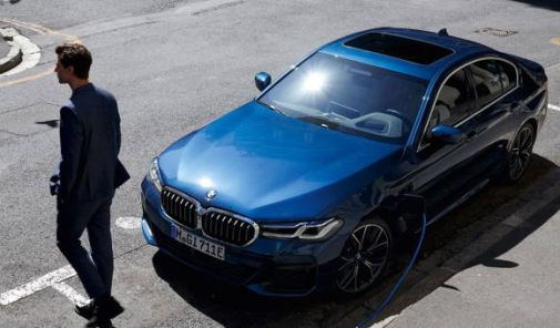 Mann in blauem Anzug steht neben an einer Ladestation angeschlossenem BMW 3er Limousine