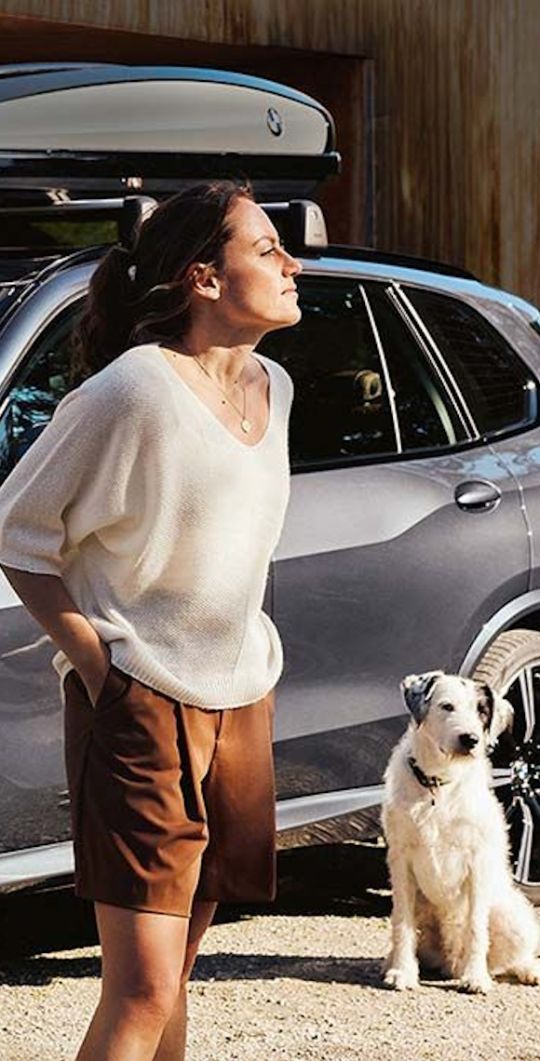 Frau mit Hund steht neben BMW Modell mit Dachbox