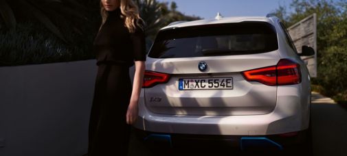 schwarz gekleidete Frau am Heck eines weißen BMW iX3