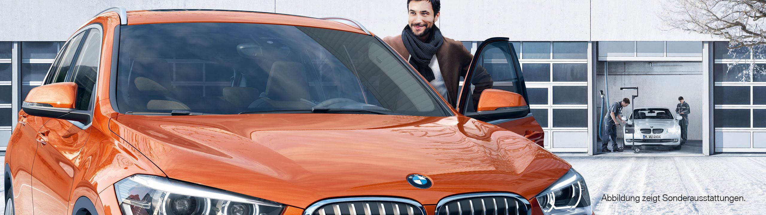 Mann steigt freudig in seinen orangenen BMW, Werkstatt in winterlicher Umgebung im Hintergrund